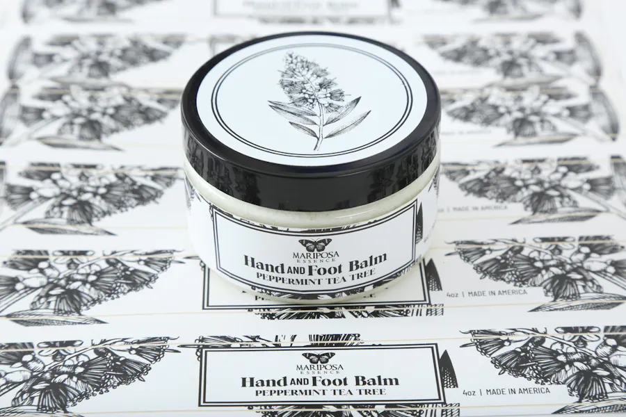 A jar of hand and foot balm sitting on top of a sheet of labels printed with Mariposa Essence and a butterfly illustration.