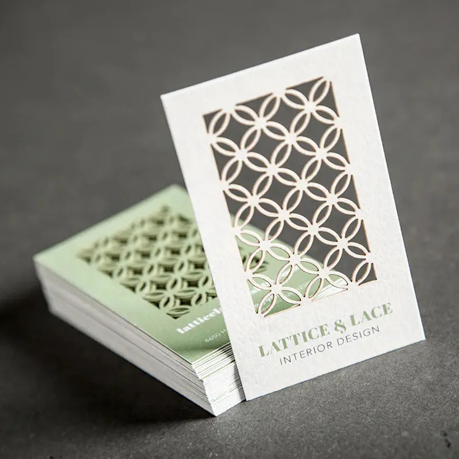 A stack of die-cut business cards printed with a lattice cutout design in cream and sage green.