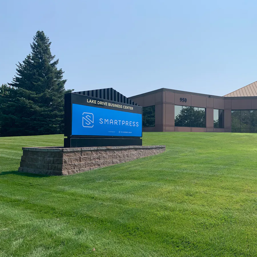 A blue outdoor business sign printed with Smartpress in white next to an office building.