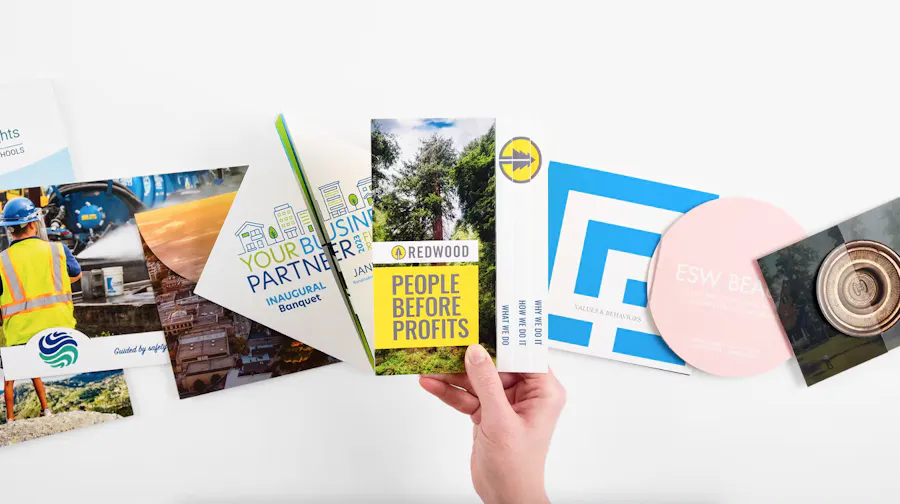 A hand holding a custom brochure above more marketing brochures in various shapes.