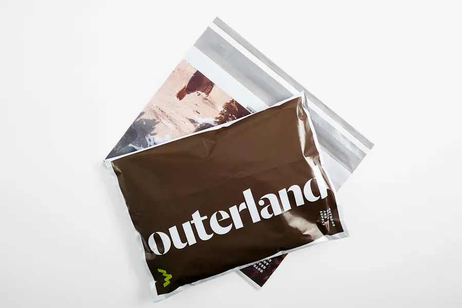 Two shipping poly bags laying on top of each other and printed with Outerland and an outdoor scene.