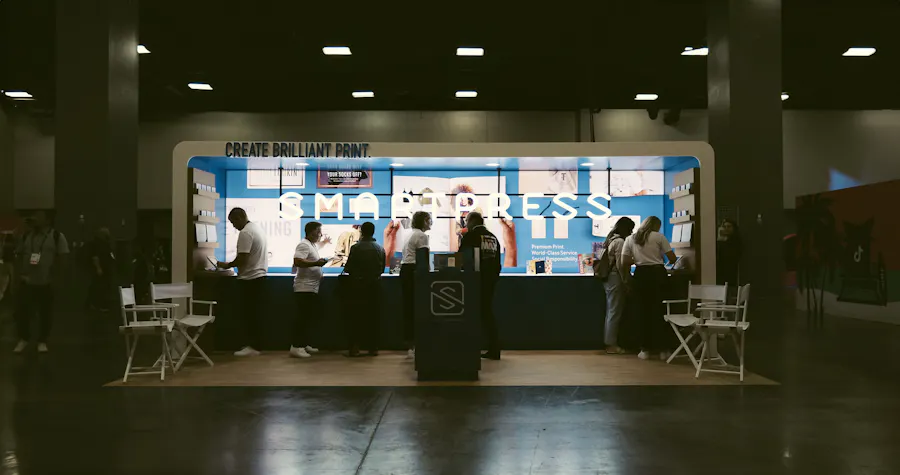 The Smartpress Adobe MAX exhibition booth with seven people standing in it looking at print samples.