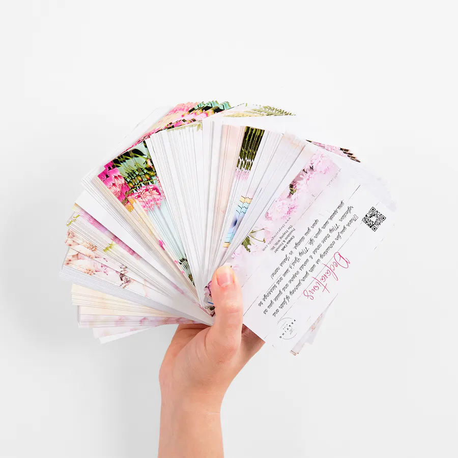 A hand holding a fanned-out deck of flashcards printed with religious content and pink floral designs.