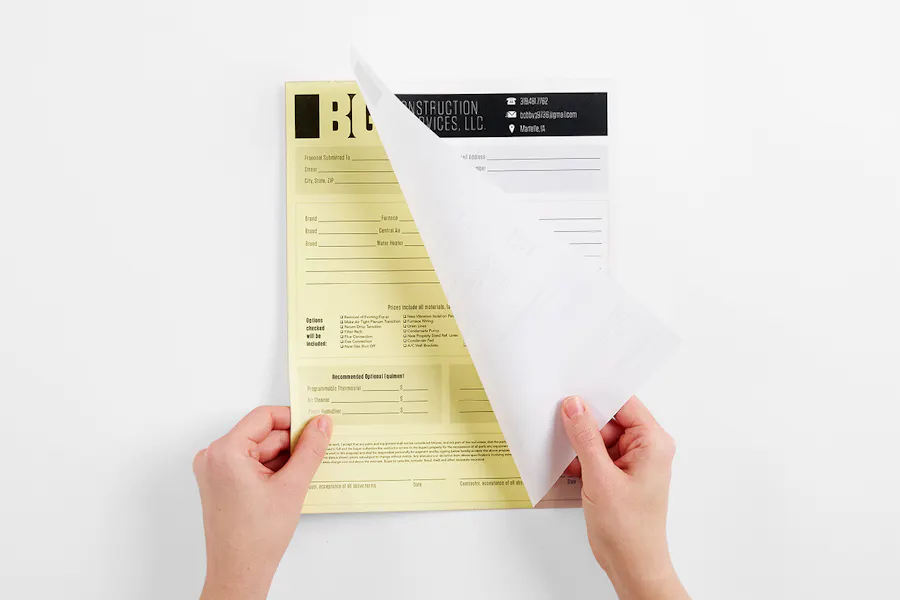 Two hands pulling apart a carbonless form printed with a construction company's proposal information.