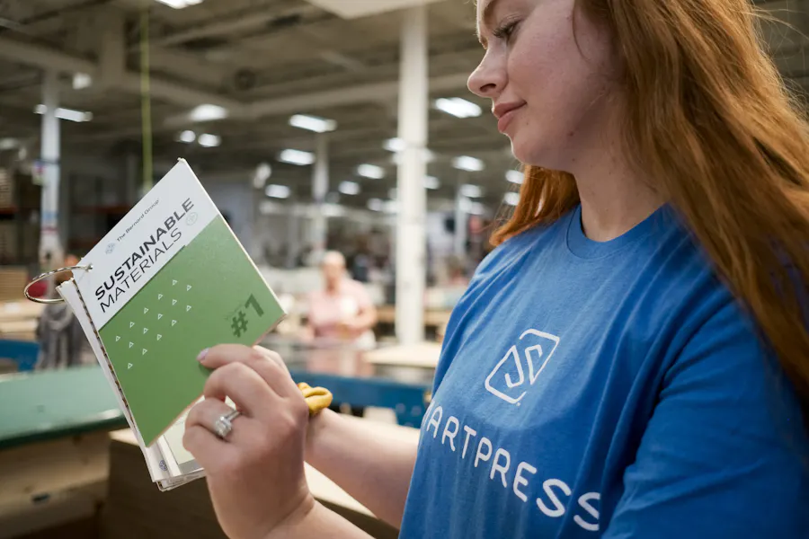 A woman wearing a blue Smartpress T-shirt and holding a flip book of sustainable material samples.