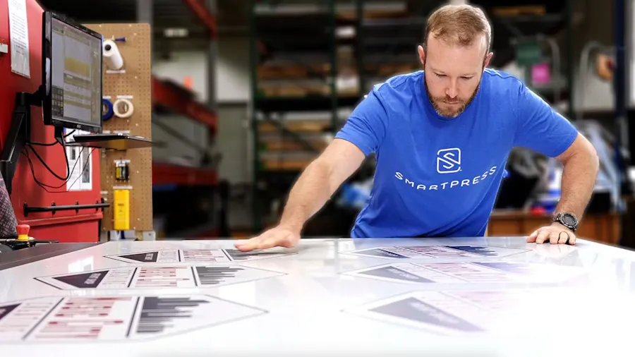 A man standing at a table in a production facility looking at custom aluminum signs.