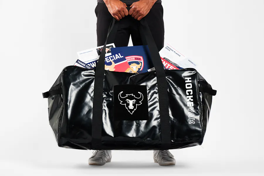 A person holding a HOCKEYAK duffel bag in front of them with printed marketing assets coming out of the main compartment.