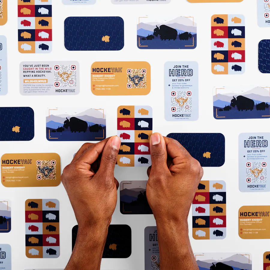 Two hands holding a custom business card printed with a repeating yak graphic above a collection of more business cards.