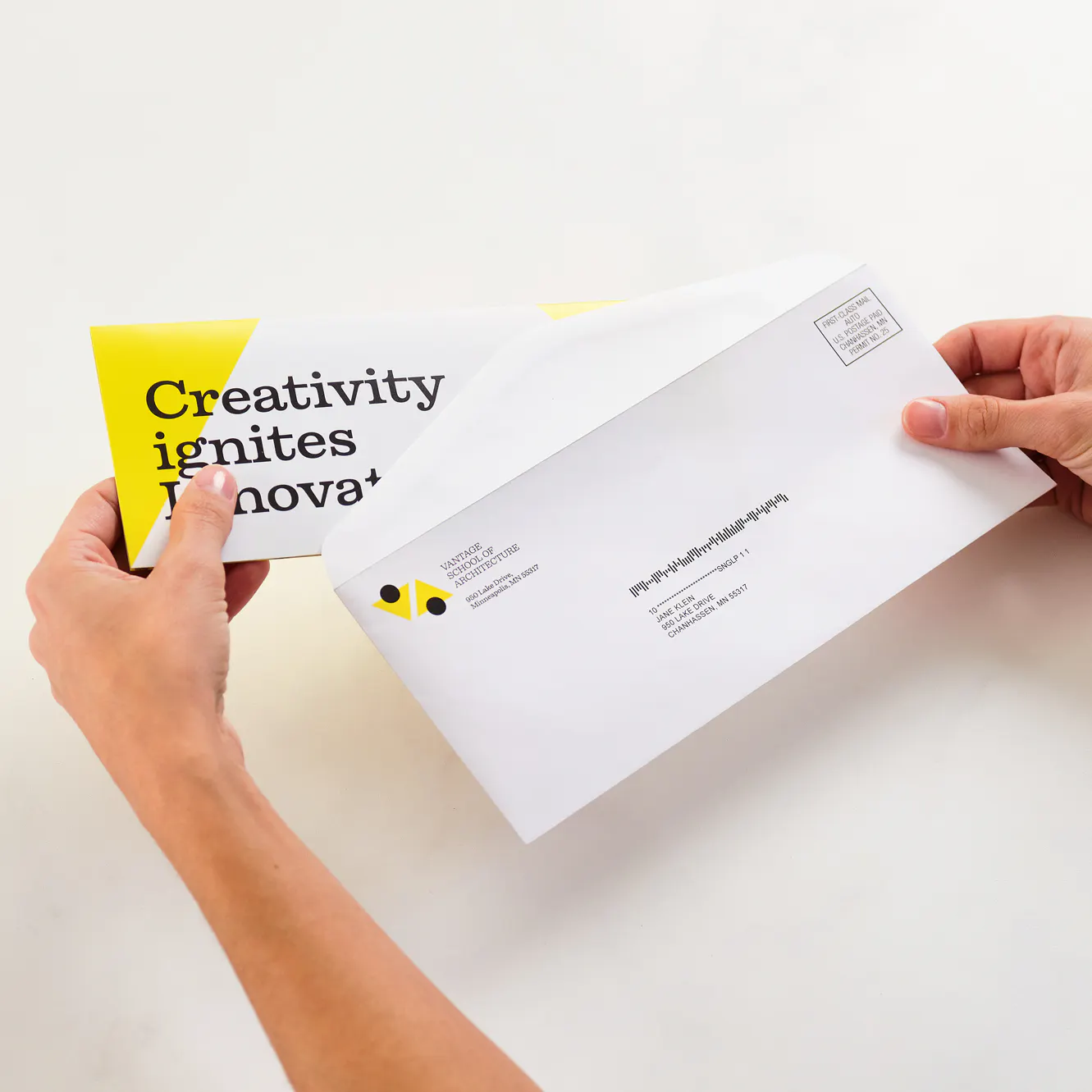 Two hands holding a letter mailer and matching envelope printed with a yellow and black design.