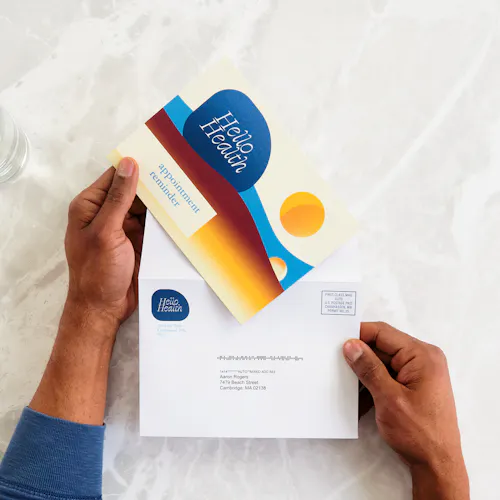Healthcare Card and Envelope Two hands holding a direct mail card and envelope printed with an appointment reminder.