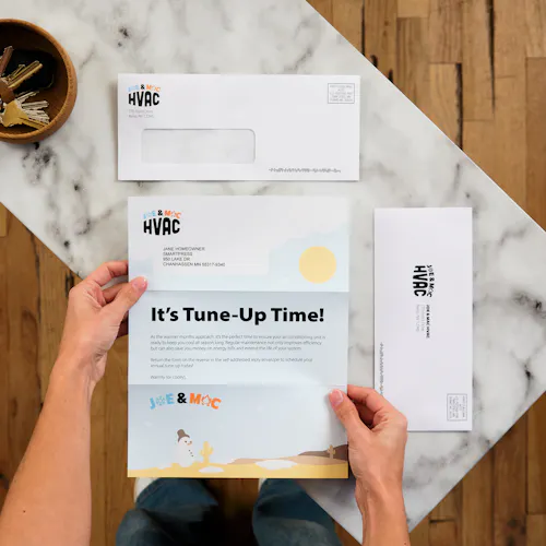 Home Services Window Letter Mailer with Reply Envelope Two hands holding an HVAC letter mailer next to a window envelope and reply envelope.