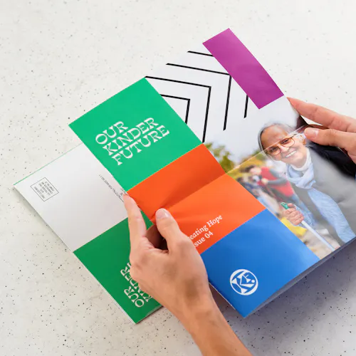 Nonprofit Newsletter Two hands holding a nonprofit newsletter printed with Our Kinder Future in orange, blue, green and pink.