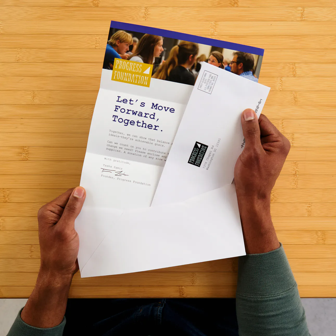 Two hands holding a letter mailer, envelope and reply envelope printed with political information.