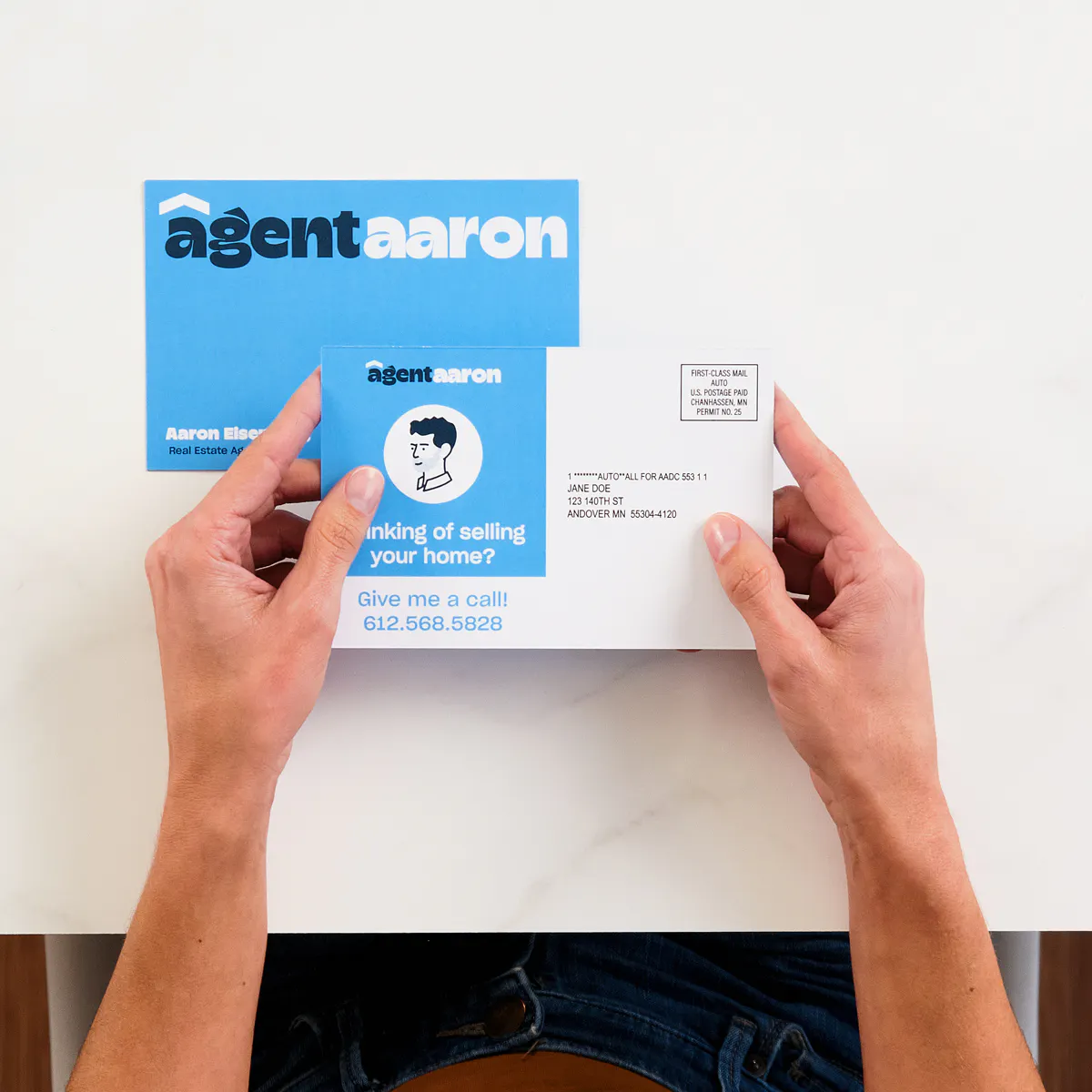 Two hands holding a real estate direct mail postcard printed with a light and dark blue design.