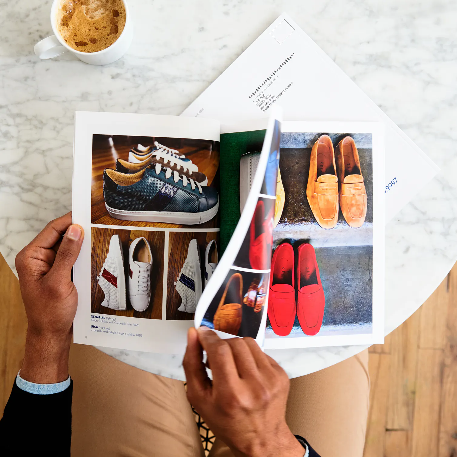 A person sitting at a table with a coffee cup and flipping through a shoe catalog.