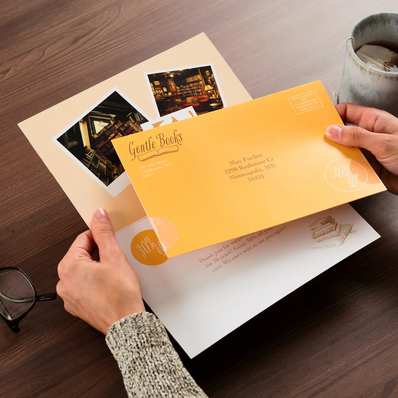 Two hands holding a folded self-mailer and envelope printed with bookstore discount info.