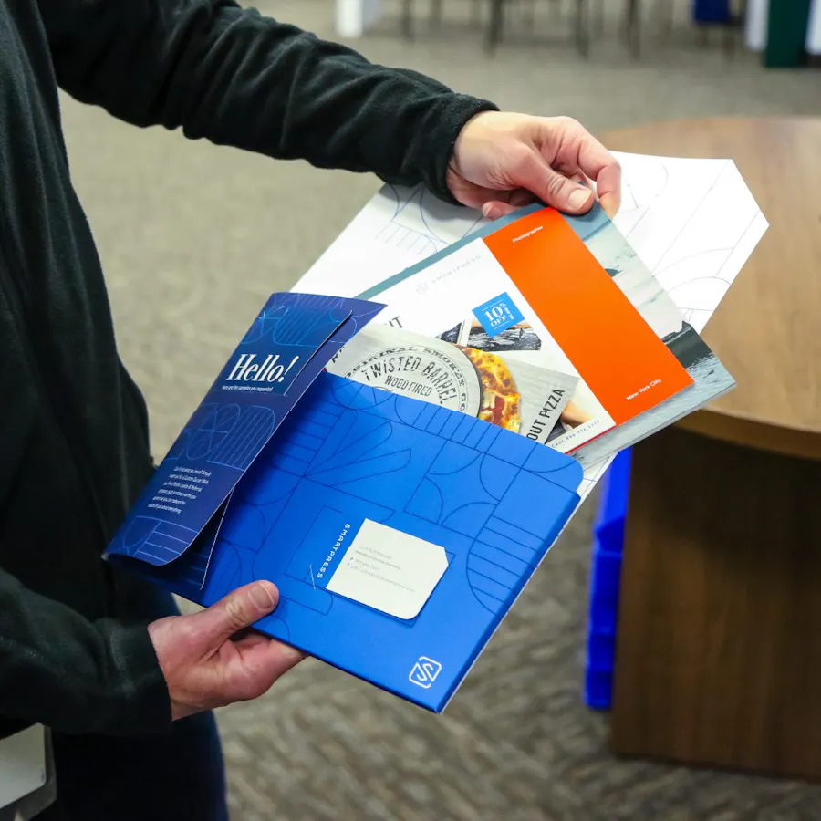 Two hands holding a branded folder printed with a blue design and pulling printed samples out of it.