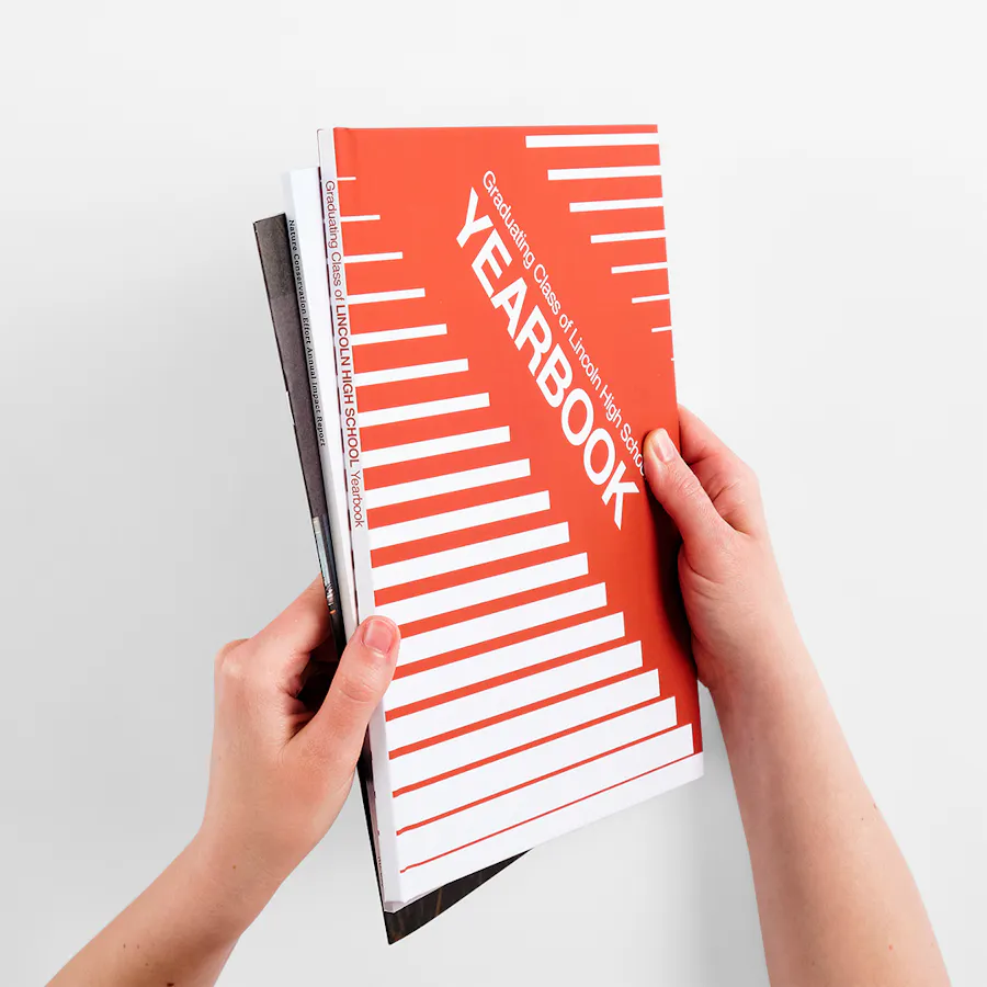Two hands holding three custom yearbooks printed with various designs.