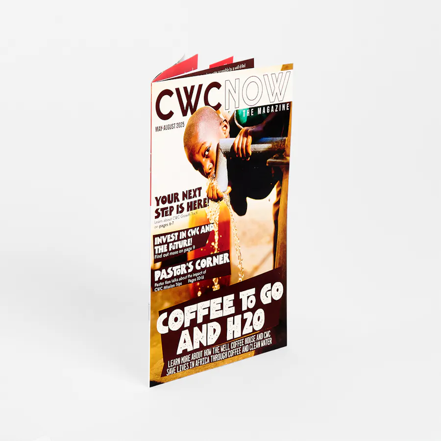 A marketing magazine standing open and printed with CWC NOW and a boy drinking from a fountain on the cover.