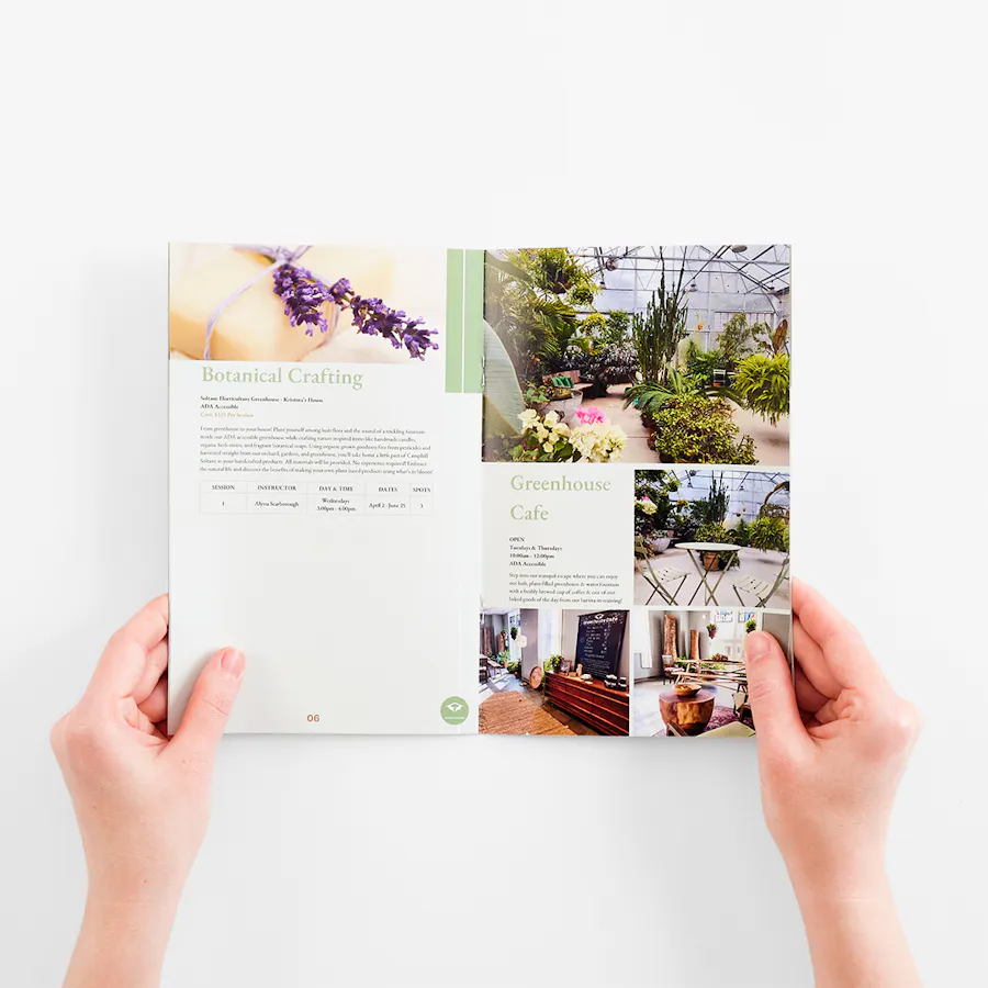 Two hands holding open a magazine printed with course information and floral imagery.