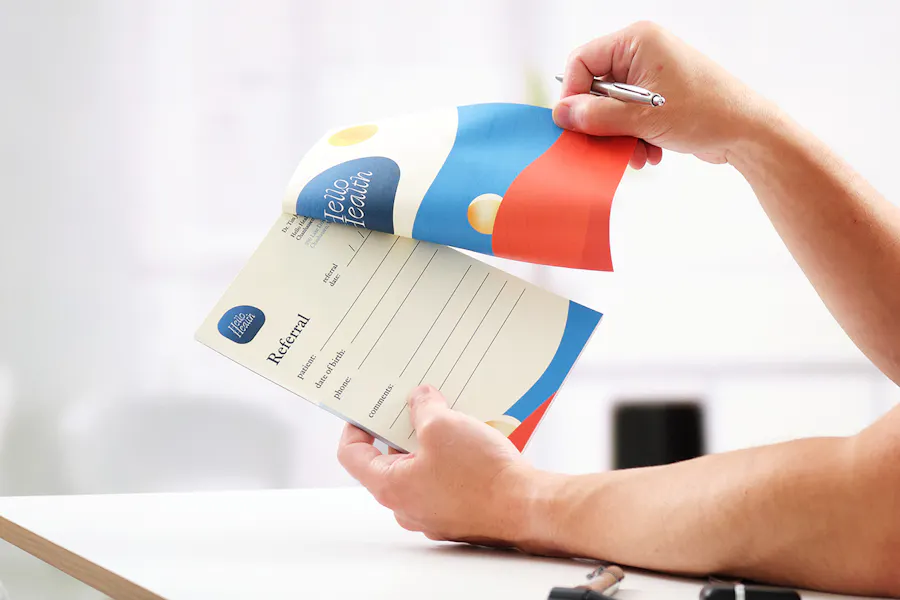 Two hands holding a medical referral pad printed with a blue and orange design.