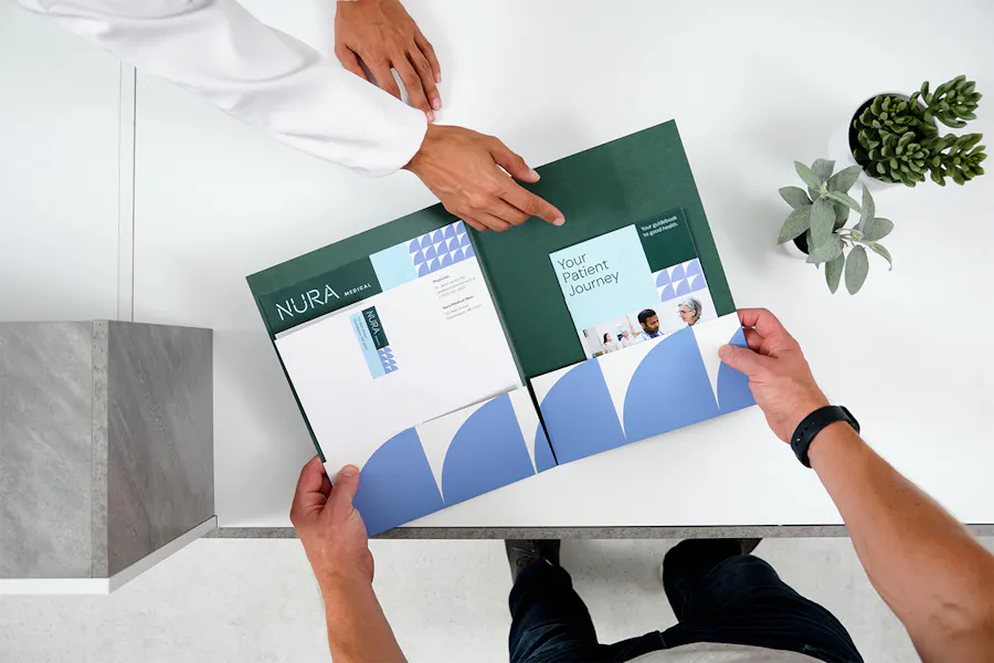 Two people looking at a pocket folder filled with health care marketing materials.