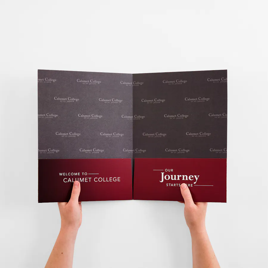 Two hands holding open a college presentation folder printed in dark gray and red.