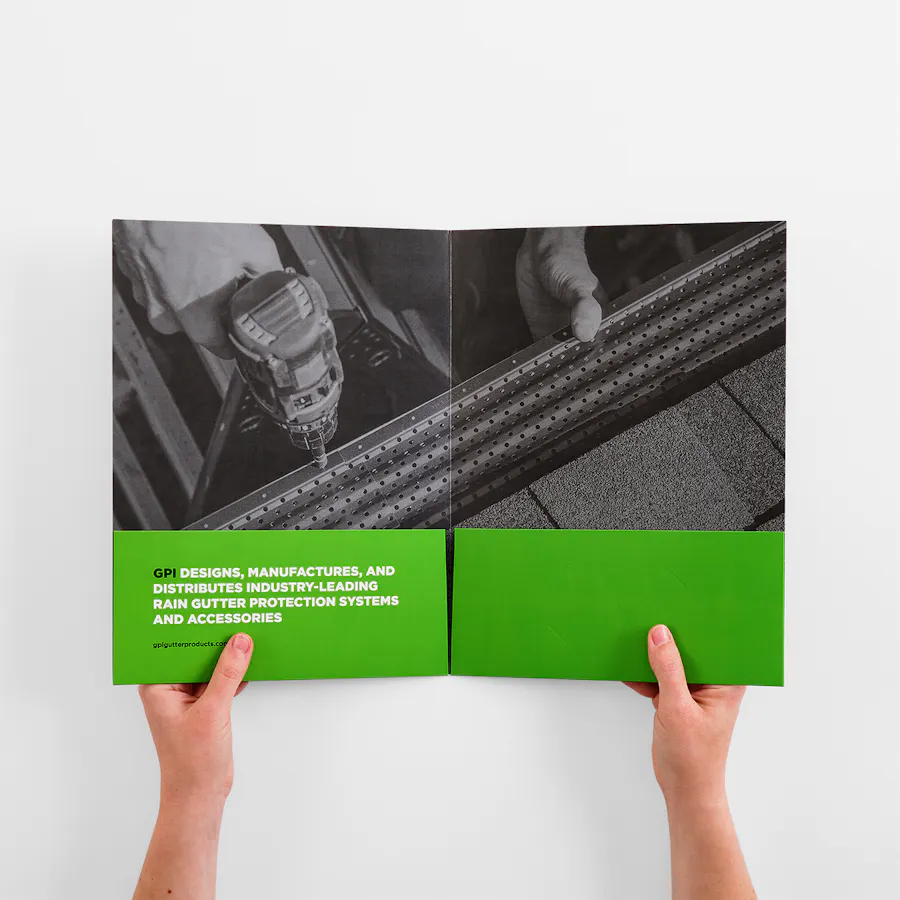 Two hands holding a pocket folder printed with images of gutter installation and green pockets.