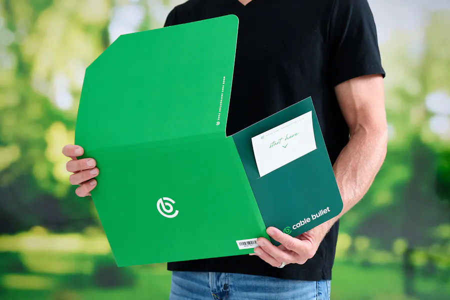 A man holding a green pocket folder printed with Cable Bullet branding.