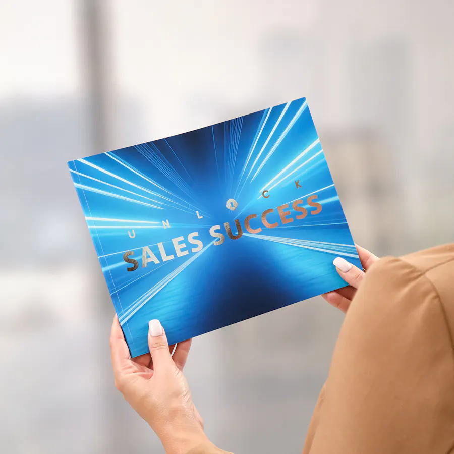 Two hands holding a sales booklet printed with a blue cover and Unlock Sales Success.