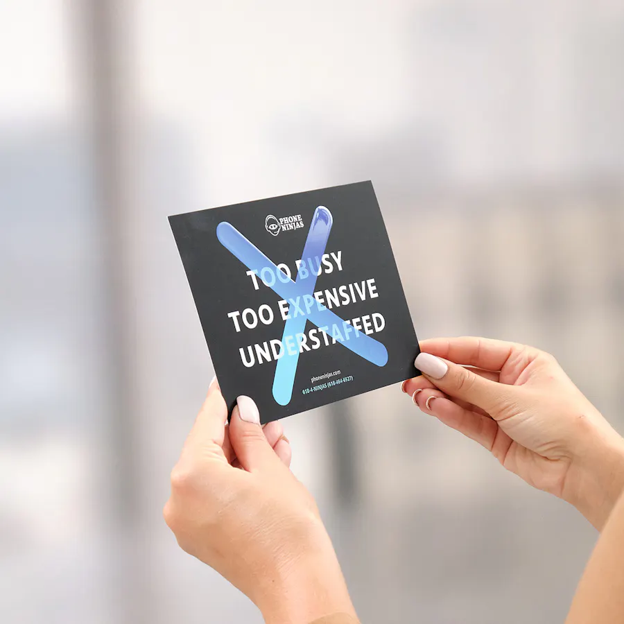 Two hands holding a custom postcard printed with Phone Ninjas marketing messaging.