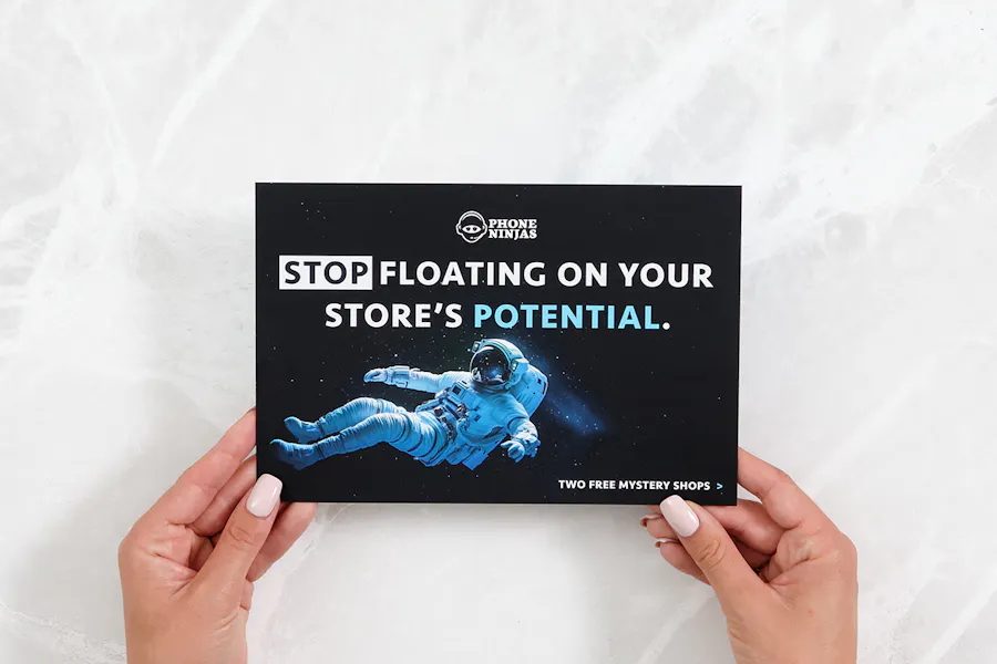 Two hands holding a marketing postcard printed with an astronaut and Phone Ninjas at the top.
