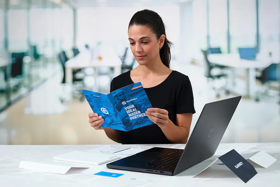 A woman looking at a Garney brochure with a laptop and other stationery around it.