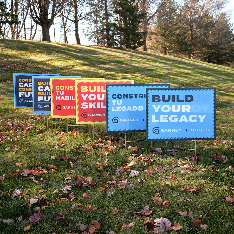 Six custom yard signs printed with Garney branding installed on a grassy hill.