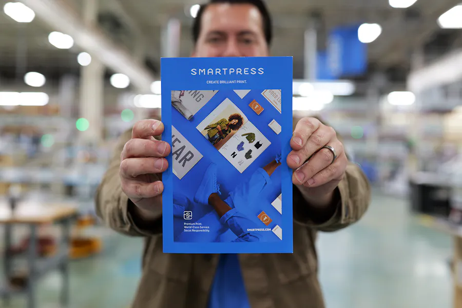 A man in a production facility holding a blue Smartpress catalog out in front of him.