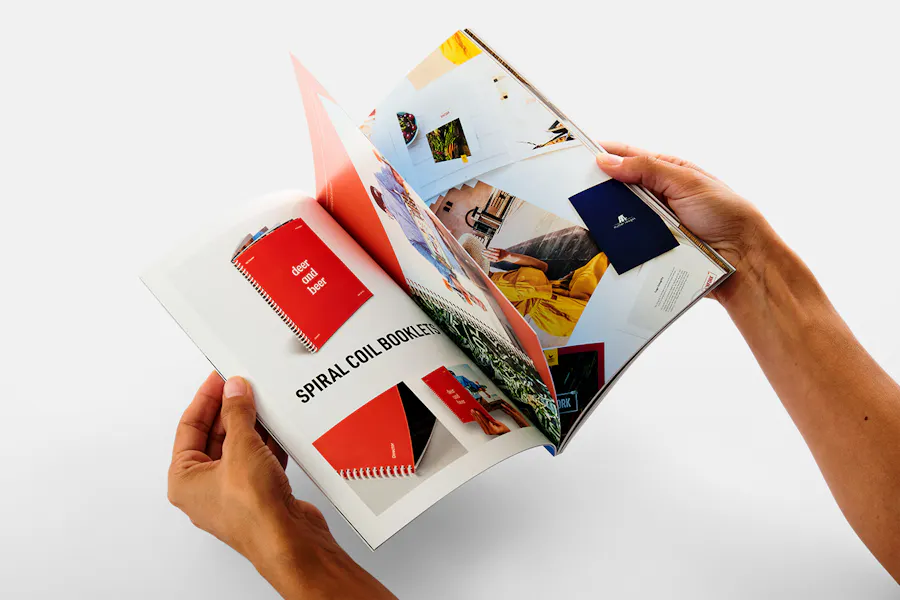 Two hands flipping through a print catalog printed with images of spiral coil booklets and other print products.