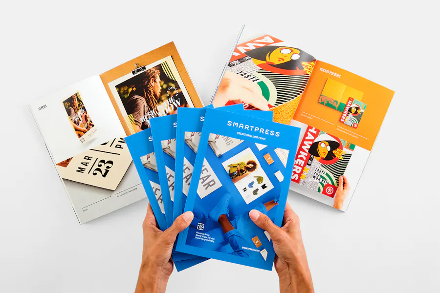 Two hands holding four catalogs fanned out above two more laying open with vibrant imagery.