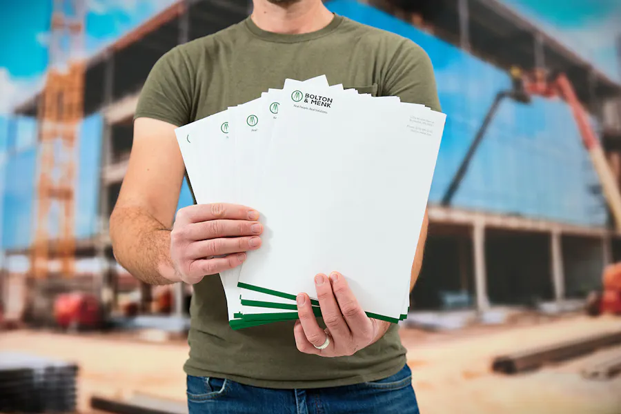 A man holding a stack of custom letterheads fanned out in front of a building construction site.