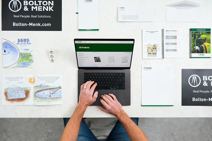 Two hands typing on a laptop with print marketing assets lined up around them on a table.
