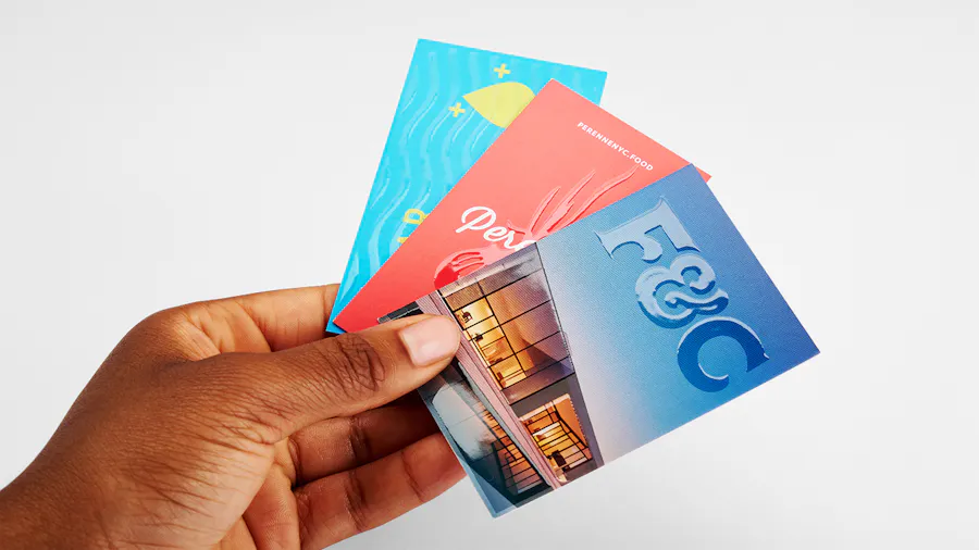 A hand holding three business cards custom printed with a raised UV coating.