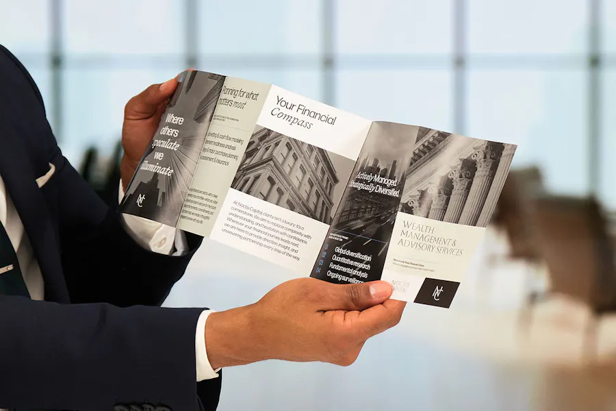 A person holding a wealth management brochure unfolded printed in black and white.