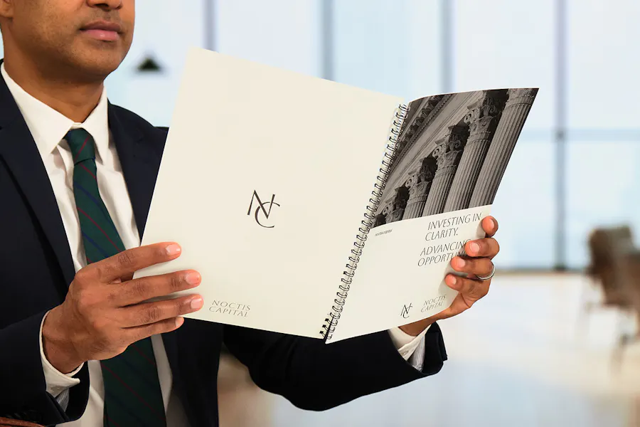 A man in a suit holding an investment guide open with a spiral binding.