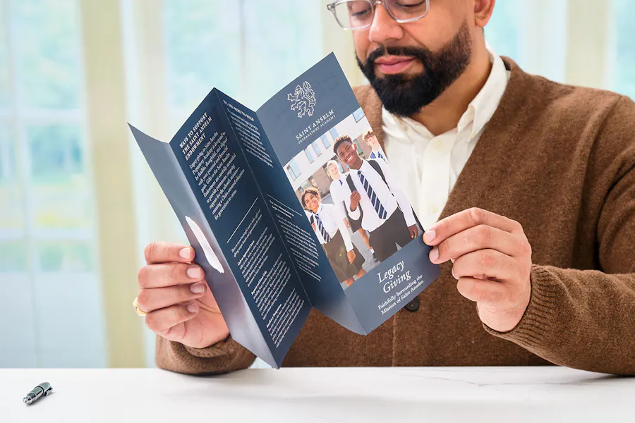 A man looking at an accordion brochure printed with Saint Anselm branding.