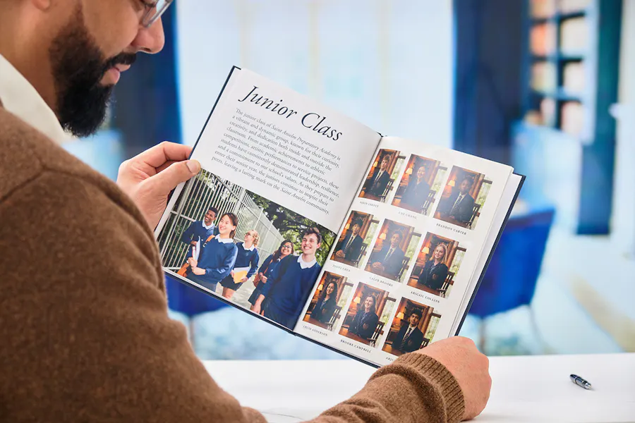 A man looking at a school yearbook printed with images of and information about the junior class.