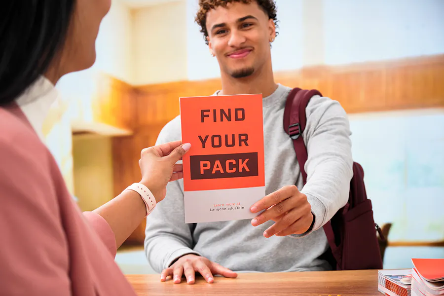 A woman handing a viewbook printed with Find Your Pack to a smiling student.