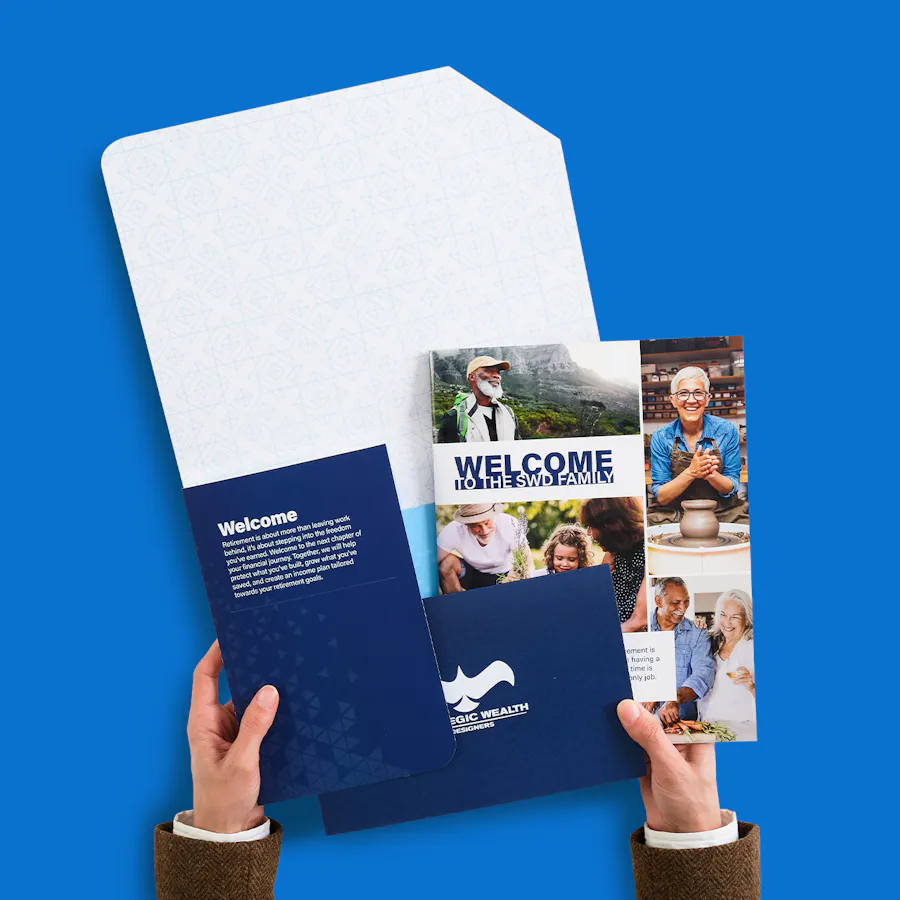 Two hands holding a printed welcome kit with two coordinating booklets for Strategic Wealth Designers.