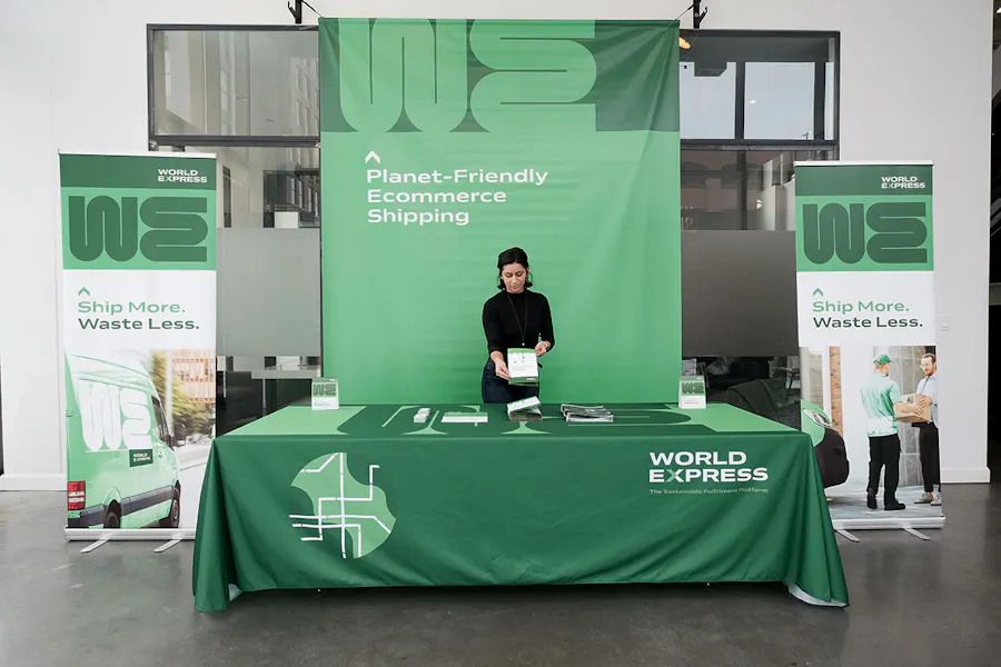 A woman standing at a trade show booth with coordinated printed banners, table cloth and brochures.