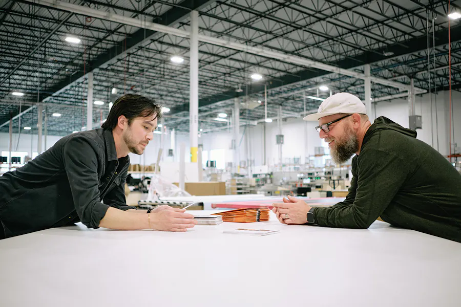 Two men leaning over a table in a print production facility looking at printed materials.