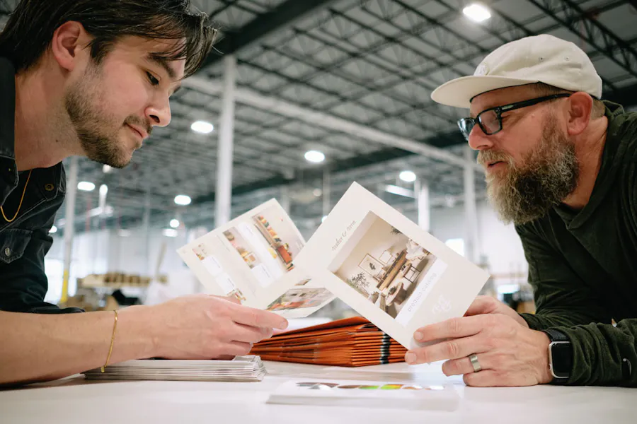 Two men leaning over a white table in a production facility holding custom printed booklets.