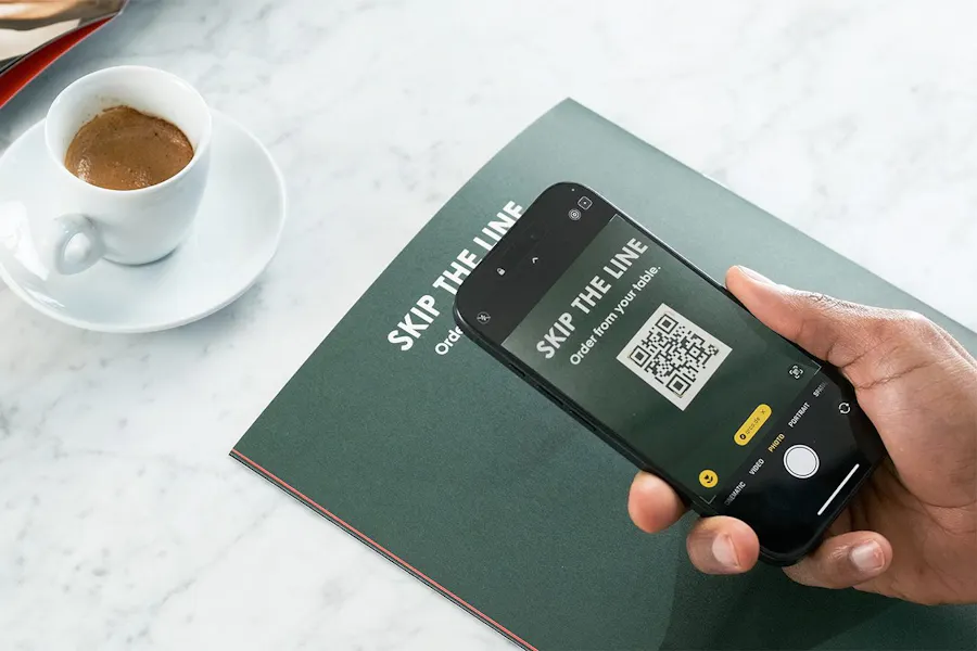 A hand holding a phone showing a QR code and skip the line in white text.